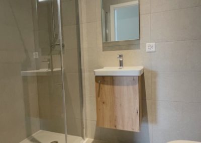 Salle d'eau équipée d'un lave main, meuble sous-vasque, miroir éclairé, grande douche et WC